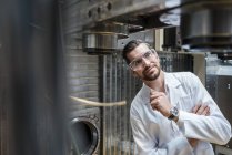 Man wearing lab coat and safety goggles at machine — Stock Photo