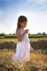Little girl standing in havested field smelling flower — Stock Photo