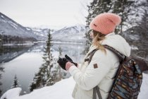 Giovane donna con cellulare nel paesaggio invernale alpino con lago — Foto stock