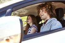 Смеющаяся молодая женщина с парнем за рулем машины — стоковое фото