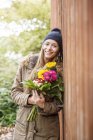Portrait of smiling young woman holding bunch of flowers outdoors — Stock Photo