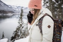 Молодая женщина по мобильному телефону в альпийском зимнем пейзаже с озером — стоковое фото