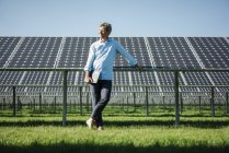 Mature man with laptop standing barefoot on meadow, solar plant — Stock Photo