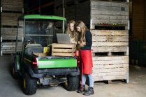Two women using laptop between crates on a farm — Stock Photo