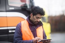 Man wearing reflective vest using tablet at trucks — Stock Photo