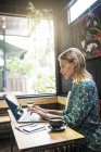 Jeune femme avec robe verte assise dans un café, travaillant sur son ordinateur portable — Photo de stock
