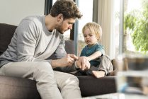 Сын осматривает отцовские часы на диване дома — стоковое фото