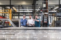 Трое мужчин делятся планшетом на заводе — стоковое фото