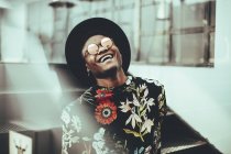 Portrait of laughing man wearing hat, sunglasses and black t-shirt with floral design — Stock Photo