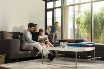 Famille sur canapé à la maison livre de lecture avec garçon sautant — Photo de stock