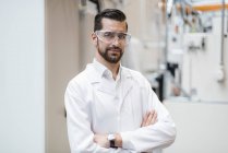 Retrato del hombre con bata de laboratorio y gafas de seguridad en fábrica - foto de stock