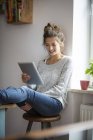 Femme souriante assise sur un tabouret et utilisant un comprimé — Photo de stock