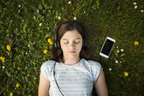 Portrait of girl lying on meadow listening music with headphones and smartphone — Stock Photo