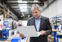 Businessman using laptop in production hall — Stock Photo