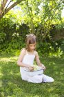 Little girl sitting on meadow in the garden with bowl of picked elderflowers — Stock Photo