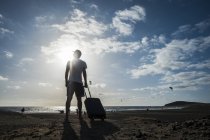 Uomo in piedi con valigia rotolante in spiaggia — Foto stock