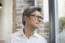 Mature businessman wearing glasses and looking out of window — Stock Photo