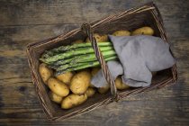 Organic green asparagus and organic potatoes in wickerbasket on wooden background — Stock Photo