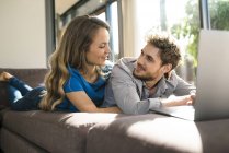 Smiling couple with laptop lying on sofa at home — Stock Photo
