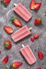 Three homemade strawberry ice lollies and strawberries on marble — Stock Photo