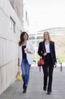 Two relaxed businesswomen with handbags and coffee to go walking on pavement — Stock Photo