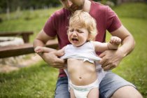 Padre vestire il suo piccolo figlio piangente in giardino — Foto stock