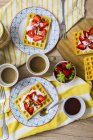 Dos platos de gofres adornados con fresas, yogur griego y almendras en la mesa de desayuno - foto de stock