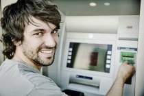 Portrait of laughing young man using cash machine — Stock Photo