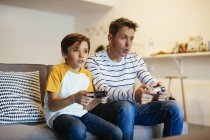 Pai e filho jogando videogame no sofá em casa — Fotografia de Stock