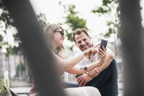 Счастливая пара, сидящая на скамейке запасных телефонов — стоковое фото
