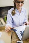 Close-up of woman at wooden desk with card and laptop — Stock Photo