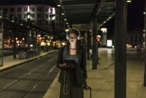Porträt einer jungen Frau mit Kopfhörer und Tablet, die nachts am Bahnhof wartet — Stockfoto