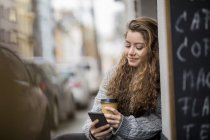 Дівчина-підліток п'є каву, читає текстові повідомлення — стокове фото