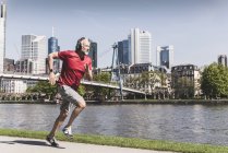 Mature man with headphones running at the riverside in the city — Stock Photo