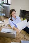 Woman sitting at desk at home with feet up and reading document — Stock Photo