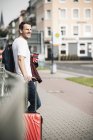 Sorrindo homem com mala rolante e café takeaway na cidade — Fotografia de Stock