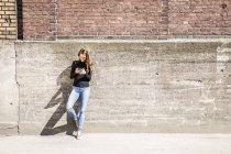 Donna con appoggiata al muro utilizzando il telefono cellulare — Foto stock