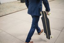 Homme d'affaires marchant avec longboard à l'extérieur — Photo de stock