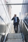Улыбающийся взрослый бизнесмен на лестнице в городе по сотовому телефону — стоковое фото