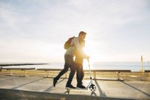 Father and son riding scooter on beach promenade at sunset — Stock Photo