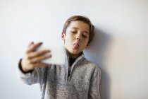 Chico tomando selfie sobresaliendo lengua contra pared - foto de stock