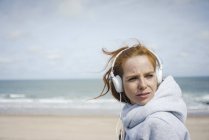 Mulher ruiva relaxando na praia, ouvindo música com fones de ouvido — Fotografia de Stock