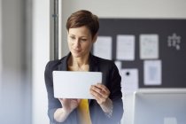 Femme d'affaires attrayante debout dans le bureau, en utilisant une tablette numérique — Photo de stock