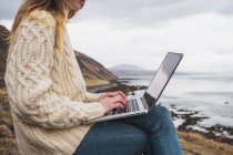 Islande, femme utilisant un ordinateur portable sur la côte — Photo de stock