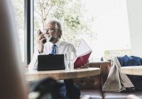 Lächelnder älterer Geschäftsmann bei der Arbeit am Tisch in einem Café — Stockfoto