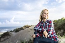 Усміхнена жінка сидить у дюнах — стокове фото