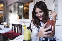 Молода жінка сидить у кав'ярні, приймаючи селфі зі смартфоном — стокове фото