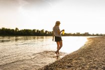 Jeune femme marchant pieds nus sur le bord de la rivière le soir — Photo de stock