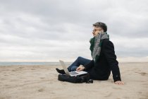 Empresario con portátil sentado en la playa en invierno - foto de stock