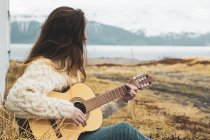 Islande, femme assise dans un paysage rural jouant de la guitare — Photo de stock